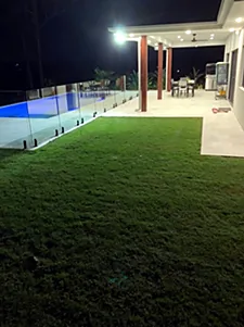 Outdoor lighting over a lawn and pool area at night