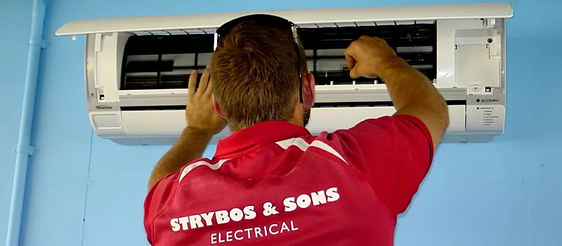 A Strybos electrician in a red uniform fitting an indoor split system air conditioner